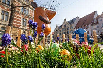 ein kleines eingezäuntes Beet mit Osterdekoration, im Hintergrund die Kika-Figuren Maus und Elefant