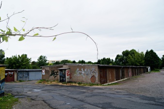 Im Mittelpunkt ein zweireihiger Garagenkomplex, die Straße davor kaputt. Links ein Ast im Bild.