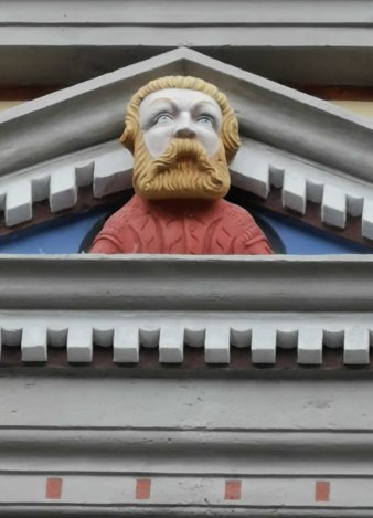 blonde Figur mit rechteckigem Vollbart in Fenstergiebel