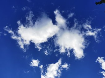 drei zarte am Rand ausgefranste weiße Wolken vor azurblauem Himmel