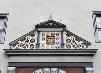 dreieckiger Giebel über Eingang, in der Mitte ein Wappen, links, rechts und oben Ornamente mit Früchten, Gesichtern