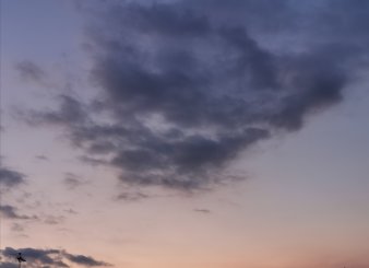 V-förmige, lockere, dunkelgraue Wolkenansammlung, unten rosa-orangene Sonnenuntergangsfarben im Hintergrund