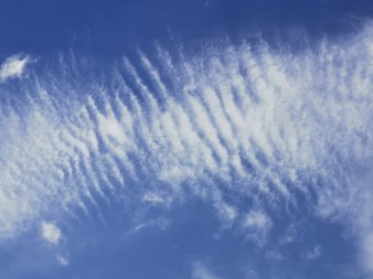 an textile Strukturen erinnerndes streifenartiges, zartes, weißes Wolkengebilde vor blauem Himmel