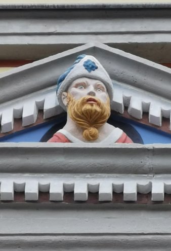 Figur mit blauweißer Kappe und langem Bart mit Knoten in Fenstergiebel