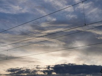 drei Wolkenschichten am Abendhimmel, vorne Straßenbahnleitungen