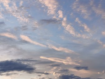 weiße Wolken streben nach links oben, unten einige schmale dunkle Wolken