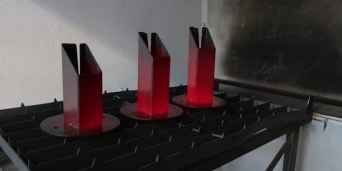 drei rotglühende stehende Vierkant-Stahlobjekte, gerade auf einem Gitterrost aus dem großen Email-Ofen gezogen