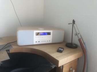 ein Radio mit weiß-grauer Front in einem Holzkorpus steht auf einem Holztisch, daneben ein Lötkolben