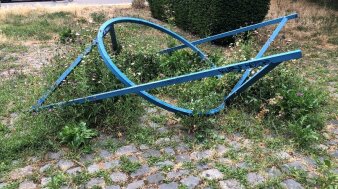Künstlerische Plastik mit geometrischen Formen in Blau auf einem gepflasterten Boden mit etwas grünem Gras