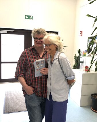 Eine Frau und ein Mann in einem weißen Zimmer stehend und lächelnd.