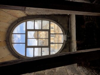 Blick durch ein Fenster auf ein buntes Haus, darüber blauer Himmel