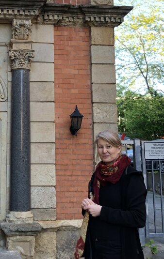 eine Frau steht vor einem flachen Gebäude, dessen Fassade eine Säule schmückt