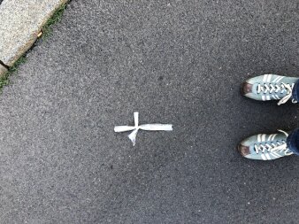 Ein weißes Kreuz auf dem Boden liegend, darunter zwei hellblaue Schuhe