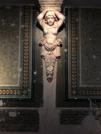 Eine nackte weibliche Figur an einer Wand hängend, daneben farbige Wandbemalungen