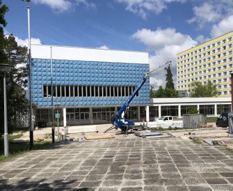 Zwei Plattenbauten, einer mit künstlerischer Fassade aus blauen Platten bzw. Waben und einem Bagger im Vordergrund