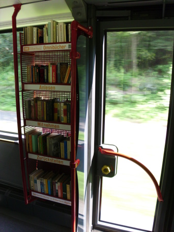Ein Bücherregal im Fahrgastraum des Busses, daneben eine glasklare Tür.