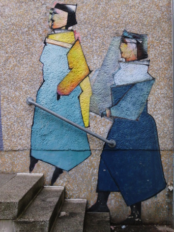 Zwei auf eine Wand gemalte Frauen steigen scheinbar die Treppe hinauf, die sich vor der Wand befindet. Beide in blauen Kleidern.
