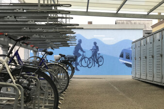 Blaues Wandbild auf dem zwei Fahrradfahrer, eine Regionalbahn und ein Linienbus gesprüht wurde