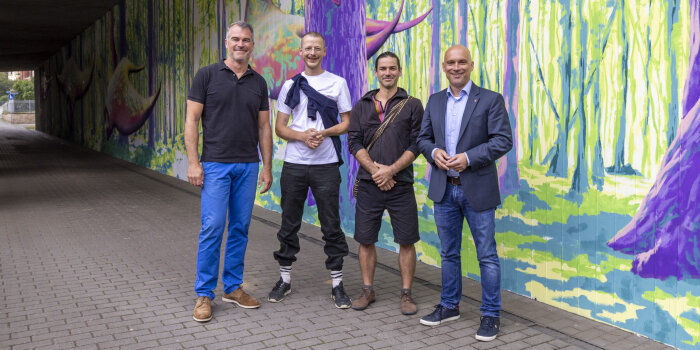 vier Männer stehen vor der bunt gestalteten Wand einer Unterführung