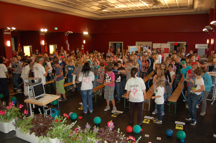 Schüler der Klassenstufe 5 warten im gefüllten Saal gespannt auf den Beginn der Veranstaltung, angeleitet durch die Mannschaftskapitäne im Vordergrund