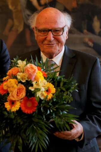 Älterer Mann mit Brille hält einen Blumenstrauß und eine Ehrenmedaille als Erfurter Ehrenbürger in der Hand.