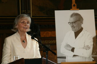 Eine Frau steht am Rednerpult im Rathaussaal und neben ihr steht eine Staffelei mit dem Bild eines Mannes.