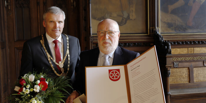 Zwei Männer bei der Ehrung zum Erfurter Ehrenbürger mit Blumenstrauß und Auszeichnung.