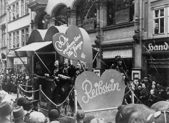 Schwarz-Weiß-Aufnahme vom Faschingsumzug in Erfurt 1937/38. Feiernde Menschen auf einem Umzugswagen in einer Straße in Erfurt. 