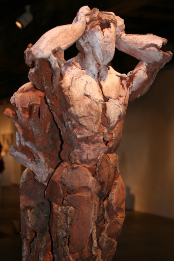 Eine Terrkottafigur blickt nach vorn rechts, die Hände hat sie über dem Kopf zusammengeschlagen. Die andere Terrakottafigur steht Rücken an Rücken zur ersten Figur.