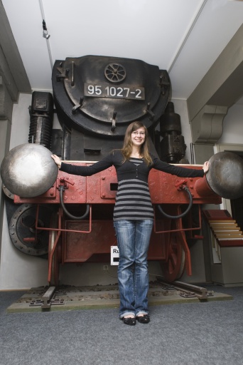 Junges Mädchen mit blazer Jeans vor der Eisenbahn. Ihre Hände hält sie zwischen den Eisenbahnpuffern.