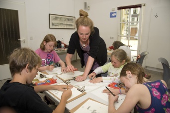 Foto: Schüler der Puschkinschule und Kursteilnehmer der Imago-Kunst-Schule © Stadtverwaltung / D. Urban Sechs Schüler unter Anleitung der Museumspädagogin, die in der Mitte steht, beim Zeichnen.