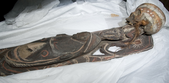 Ein geschnitztes Holzbrett mit Bemalung, rechts ein Schädel.