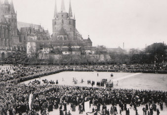 Auf dem Platz im Carré zahlreiche Menschen. Dahinter die Silhouette vom Katholischen Dom St. Marien und der Kirche St. Severi.