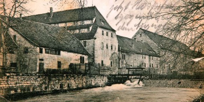 Foto: Jenseits des vormaligen Wehrgrabens lebt man im Großen Hospital in einem eigenen Kosmos: Spittelwehr, Herrenhaus und Steinhaus. Ansichtskarte "Alt-Erfurt", um 1890 © Museum für Thüringer Volkskunde Erfurt Häuserzeile, davor ein Fluss mit Wehranlage.