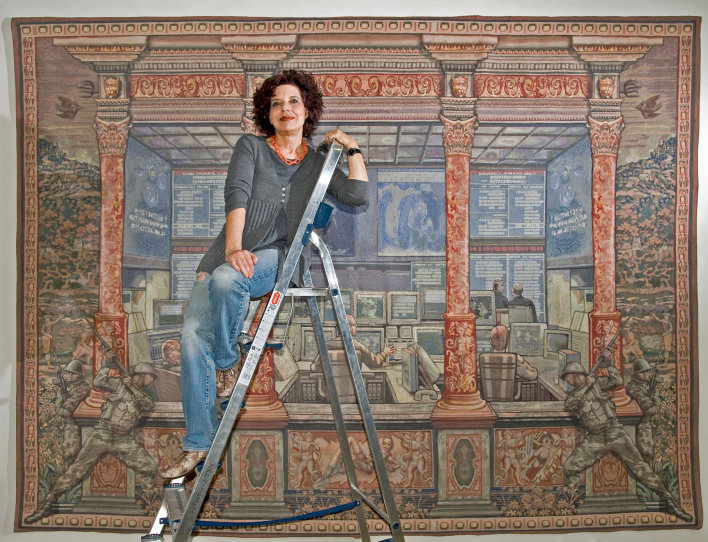 Foto: Margret Eicher im Angermuseum vor ihrer Arbeit Herrscher der Welt, digitale Montage/ Jaquard Gewebe, 265 x 360 cm © Stadtverwaltung Erfurt / D. Urban Eine Frau auf der Leiter. Im Hintergrund ein Wandtgeppich.