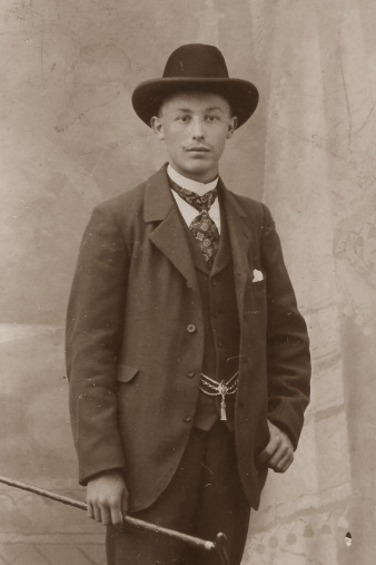 Ein junger Herr im Anzug mit Hut und Stock in der Hand.