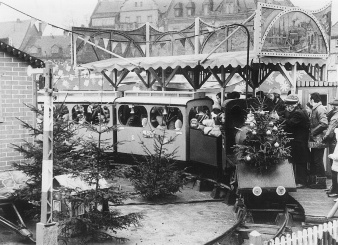 Eine im Kreis fahrende Bahn. Auf der Lokomotive ein mit Kugeln geschmückter Baum. In der Mitte des Kreises drei ungeschmückte, kleine Tannen.