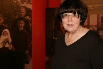 Dame mit Brille und schwarzem Shirt vor einer Ausstellungswand.