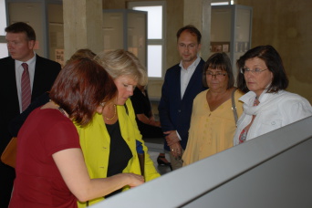 Foto: Annegret Schüle führt die Kulturstaatsbeauftragte Monika Grütters (Mitte) durch die Ausstellung. Unter den aufmerksamen Zuhörern: Kulturdirektor Knoblich, Bürgermeisterin Thierbach und die Bundestagsabgeordnete Tillmann (v. l. n. r.). © Stadtverwaltung Erfurt / Erinnerungsort Topf & Söhne" Verschiedene Personen schauen in eine Vitrine.