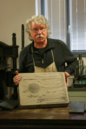 Ein Mann mit Druckerschürze hebt eine Steindruckplatte an.
