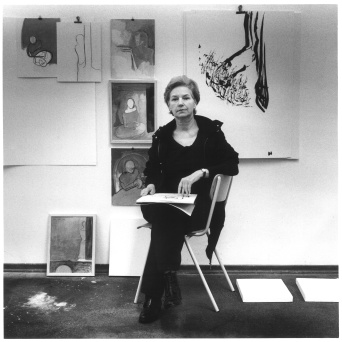 Eine Frau auf einem Stuhl sitzend, im Hintergrund deren Werke.