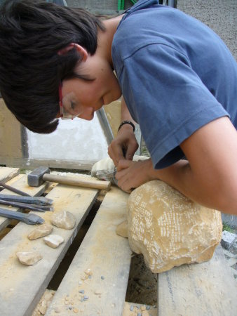 Jugendlicher arbeitet an Steinskulptur.