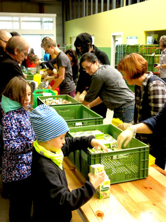 Menschen an einem langen Tisch, die beim Einpacken helfen.