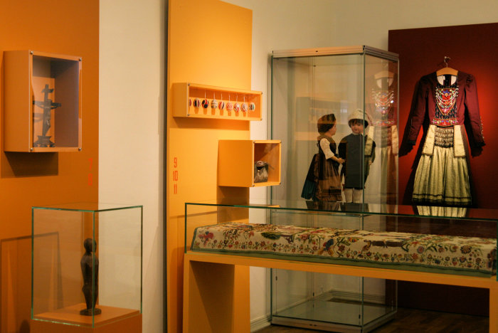 Farblich gestaltete Ausstellung in Rot- und Gelbtönen, inklusive Glasvitrinen.
