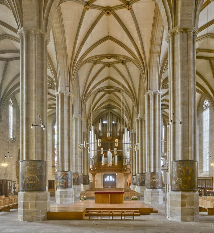 Der Pfeilerbildzyklus im Katholischen Dom St. Marien Altarinsel im Inneren einer Kathedrale, rechts und links davon mehrere Pfeiler, auf denen sich im jeweils unteren Teil halbrunde Gemälde befinden.