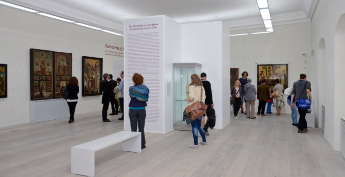 Foto: Ausstellung "Kontroverse und Kompromiss: Der Pfeilerbildzyklus des Mariendoms und die Kultur der Bikonfessionalität im Erfurt des 16. Jahrhunderts" © Falko Behr Menschen in einem Ausstellungssaal