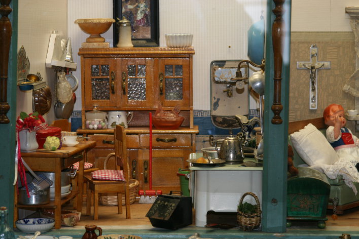 Foto: "Die Welt im Kleinen" war Thema einer Ausstellung, die 2010 im Museum für Thüringer Volkskunde Erfurt präsentiert wurde. Puppenhäuser, Puppenstuben, Puppenküchen und Kaufläden aus der Sammlung Steffi Rebettge-Schneider wurden von zahlreichen Besuchern betrachtet. © Stadtverwaltung Erfurt / S. Glaubrecht Puppenküche und Puppenwohnzimmer mit Küchenbuffet, Tisch, Stuhl, Herd und Kruzifix über dem Chaiselongue.