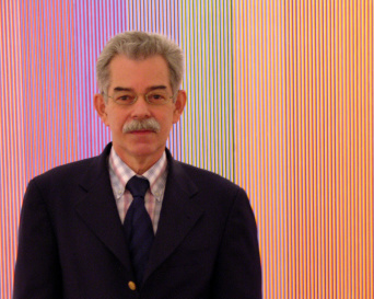 Herr mit Brille und Krawatte vor einer in bunten Farbstreifen gestaltetetn Wand.