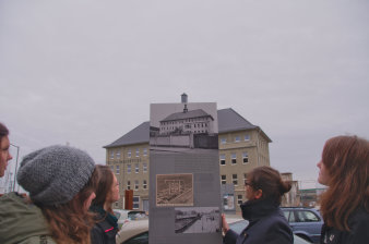 Schüler stehen vor einer Informationstafel, dahinter ein Verwaltungsgebäude.