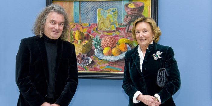 Eine Dame rechts, ein Herr links, in der Mitte ein farbenfrohes Gemälde.